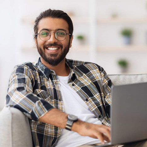 Ein Mann mit Bart lächelt, während er ein Laptop auf dem Schoß hält.