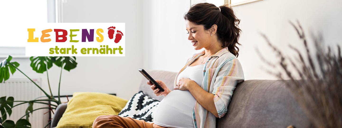 Eine Schwangere sitzt auf ihrem Sofa und schaut auf ein Smartphone